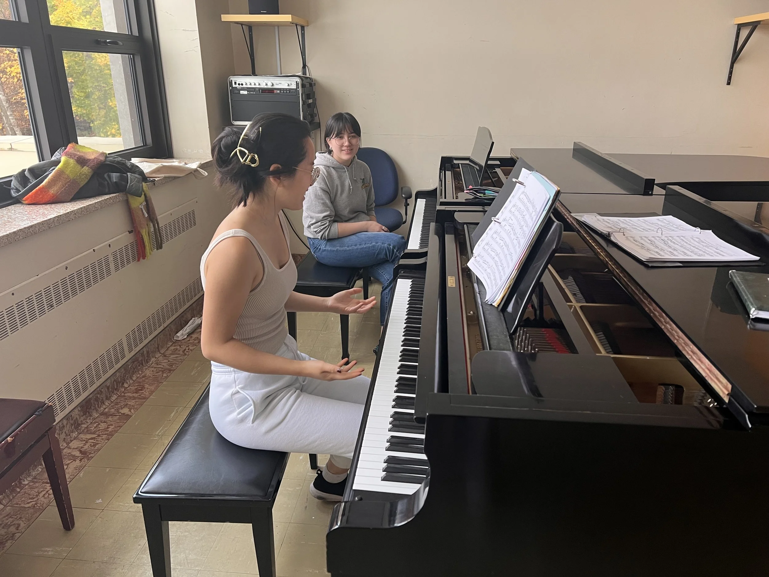 Fiona Wu working with a student at a grand piano in a sunlit teaching studio
